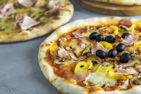 baked pizza with, ham, olives, bell pepper, tomato sauce, topped with melted cheese, on a wooden table, on a background of bakingの写真素材