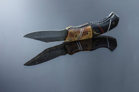 folding pocket knife on a mirrored surface, blade made of multi-layer Damascus steel, handle made of...