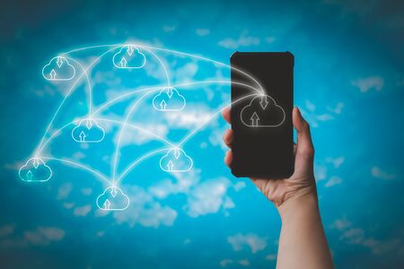 Hand holding smartphone with cloud icon on blurry blue sky background. Communication of business and financial. Cloud data storage concept.の写真素材