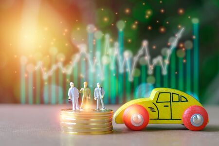 Group of engineer Miniature people, small model human figure standing on stack of golden coins and wooden yellow car  with green bokeh background. Copy space for your text. Business and financial concept.の写真素材