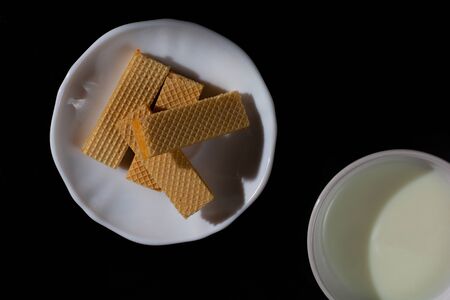 Top view four wafer in white plate with cup of milk on black background with copy space.の写真素材