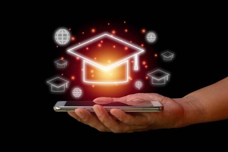 E-learning concept. Hand hold smartphone with  transparent mortar board  and earth icon on black background.の写真素材