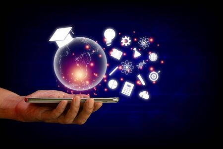 E-learning concept. Hand hold smartphone with  transparent earth and white education icon on blue technology background.の写真素材