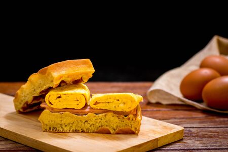 Waffle sandwich with egg and chicken ham on chopping board on wooden table and black background....