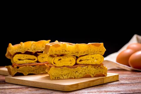 Waffle sandwich with egg and chicken ham on chopping board on wooden table and black background....