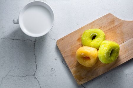 Vanilla and pandan doughnut on wooden chopping board with cup of hot milk. Breakfast concept.の写真素材