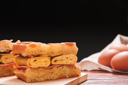 Waffle sandwich with egg and chicken ham on chopping board on wooden table and black background. Homemade food concept.の写真素材