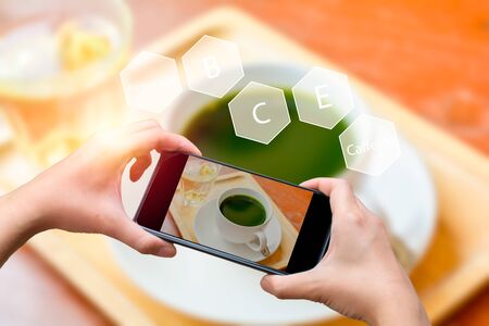 Healthy beverage concept. Topview handhold smartphone use application to calculate the nutrients in a cup of hot green tea on a wooden table in a restaurant.の写真素材