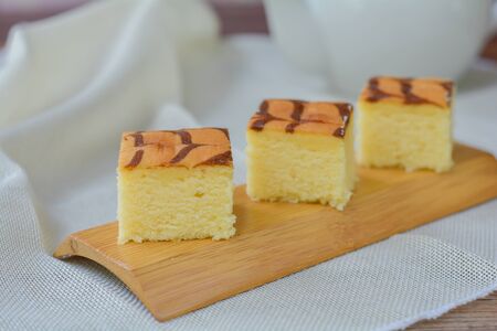 Cube cut of butter cake on wooden tray and table for served in party. Delicious dessert eat with tea and coffee in morning.の写真素材
