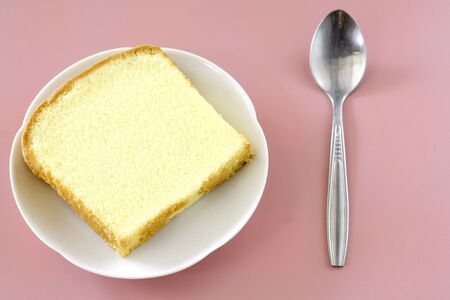 Square cut of vanilla butter cake in white dish on pink background.
