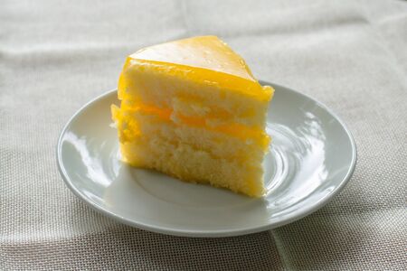 Delicious slice of orange cake served on white dish in coffee times on tablecloth.の写真素材