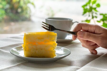 Eatting slice orange cake with metal fork served on white plate on table cloths in coffee times with green nature bokeh light background.の写真素材