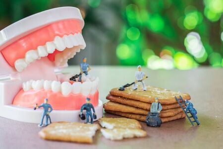 Group of teamwork miniature people, small model human figure cleaning crackers and denture on wooden...