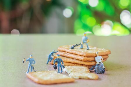 Group of teamwork miniature people, small model human figure cleaning crackers on wooden table with...