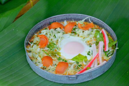 Delicious egg pan with sausage ,crab stick, cabbage and lettuce in small metal pan on green banana leave. Healthy breakfast in morning.の写真素材