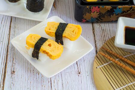Tamagoyaki sushi or sweet egg on rice and seaweed wrap on square white plate. Delicious japanese food.の写真素材