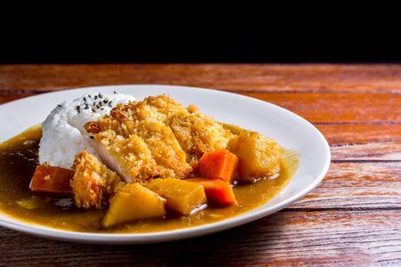 Japanese curry with rice, black sesame, carrot, potato and deep fries chicken in white dish on wooden table.の写真素材