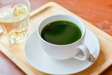 Set of hot matcha (green tea) in white ceramic cup served on wooden tray on table in cafe and coffee...