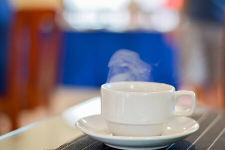 Hot coffee and tea in white ceramic cup on plate with smoke in blurry background.の写真素材