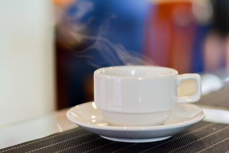Hot coffee and tea in white ceramic cup on plate with smoke in blurry background.の写真素材