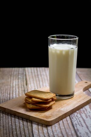 Fresh milk in glass serve with square of cracker on wooden tray with copy space for your text. Healthy beverage concept.の写真素材