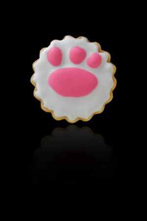 Cat footprint shape of icing cookie on black background. Beautiful delicious bakery for gift in...
