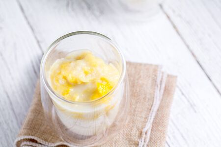 Summer appetizer of Thailand concept. Durian and sticky rice with coconut milk cream in transparent glass on white wooden table and brown table cloth. Famous street food in Thailand.の写真素材