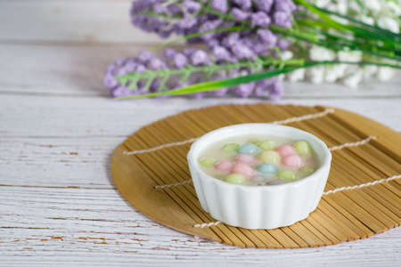 Color rice dumpling in coconut milk (Bua Loy) in white bowl on wooden table with purple flower. Delicious Thai dessert.の写真素材