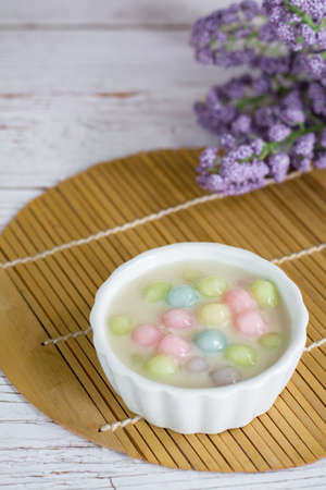 Color rice dumpling in coconut milk (Bua Loy) in white bowl on wooden table with purple flower. Delicious Thai dessert.の写真素材