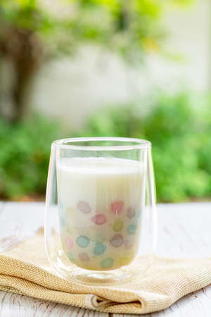 Color rice dumpling in coconut milk (Bua Loy) in white bowl on wooden table with purple flower. Delicious Thai dessert.の写真素材