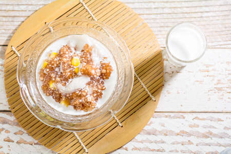 Thai dessert concept. Tapioca pearls form sago three with coconut milk, corn and young coconut in transparent bowl on wooden table.の写真素材