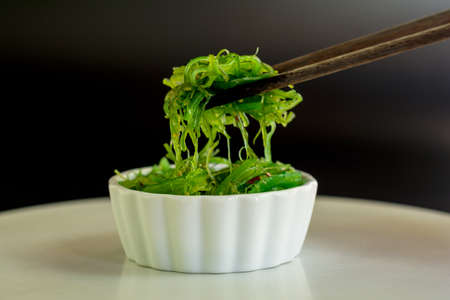 Japanese food concept. Fresh seaweed salad with sesame seeds in white bowl on black background.の写真素材