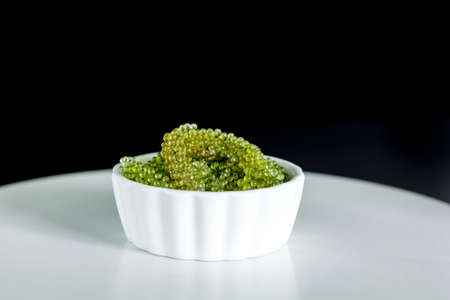 Fresh sea grapes or caviar seaweed in white bowl on wooden mat and black background. Healthy food concept.の写真素材