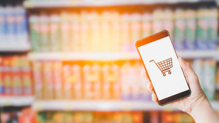 Shopping online concept. Hand holding black smartphone and white blank screen in blurry at shopping...