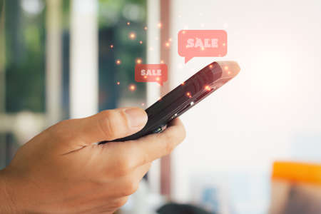 Shopping online concept. Hand holding black smartphone with red popup sale. Black Friday and shop at home.の写真素材