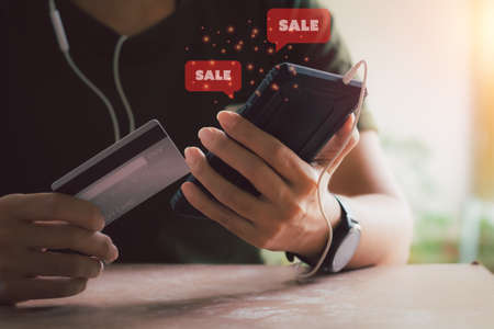 Shopping online concept. Hand holding black smartphone with red popup sale icon and credit card....