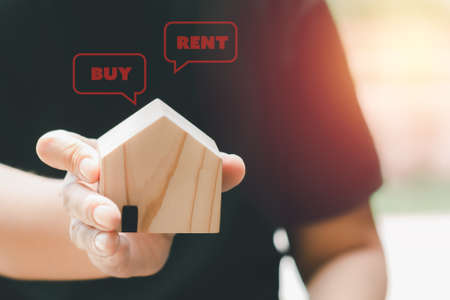 Choice between of buy or rent. Hand holding a small wooden home with red pop up of buy or rent house. Business concept.の写真素材