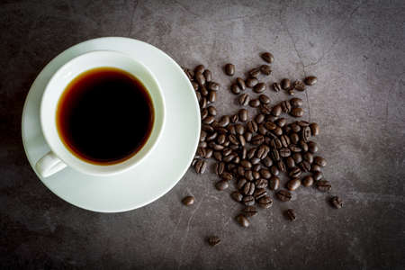 Refresh and energy drink concept. Hot black coffee or espresso in a white ceramic cup and coffee beans on a dark stone table.の写真素材