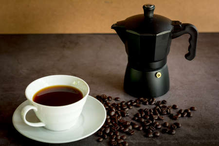 Business concept. Black coffee or hot espresso in a white ceramic cup and hand hold white screen on a smartphone or mobile on a dark table.の写真素材