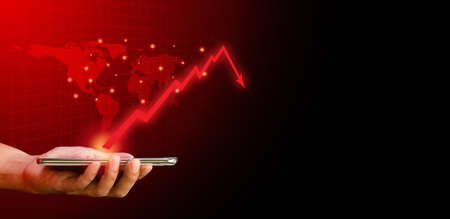 Hand holding mobile or smartphone with red arrow graph drop arrow down with world map on red background. Money losing. Stock crisis and finance concept.の写真素材