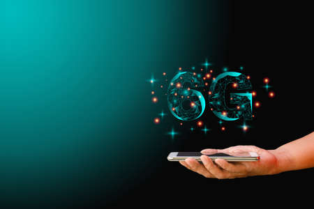 Mobile phone data technology and telecommunication global network concept. Hand-holding mobile or smartphone with low polygon dot connect line shape of 6G on dark background.の写真素材