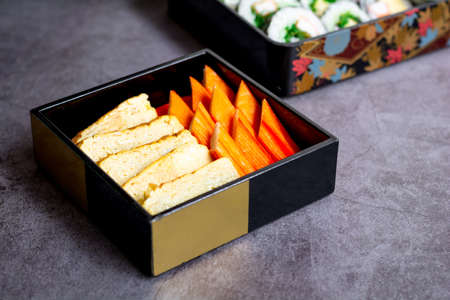 Tamagoyaki (Japanese omelet) or sweet egg with crab stick in the box set bento on a dark table. Delicious Japanese food.の写真素材