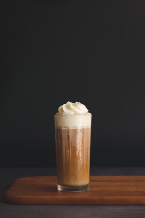 Ice cappuccino with whipping cream on a wooden table with a black background. Time to served coffee.の写真素材