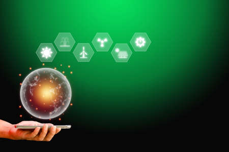 Hand holding smartphone and transparency earth with energy resources icon, on a green background. Energy concept.の写真素材