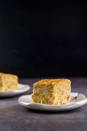 Close up square cut of homemade sweet and soft carrot cake on white plate on table. Delicious and...