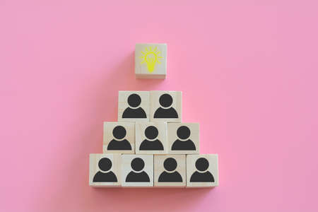 Teamwork and creative thinking and innovation concept. The pyramids of wooden blocks with human icons and bright light bulbs on a pink background. Collaboration of people in the organization.の写真素材