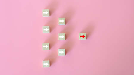 Leadership concept. The white arrows on wooden blocks and red arrows lead the way on pink background. Business start-up. Different thinking for discovering new technology and business opportunity.の写真素材