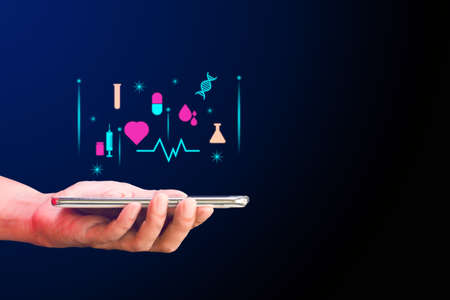 Telemedicine, medical technology, online healthcare concept. Hand holding smartphone or tablet with health icon on virtual screen on blue background. Copy space for text.の写真素材
