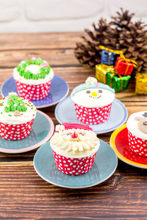 Christmas bakery concept. Cupcake with buttercream and topping, Santa Claus, Rudolf, and a Christmas tree on a wooden table.の写真素材