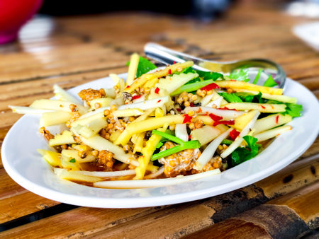 Coconut shoot spicy salad with horseshoe crab egg on white dish and wooden table. Thai delicious food.の写真素材